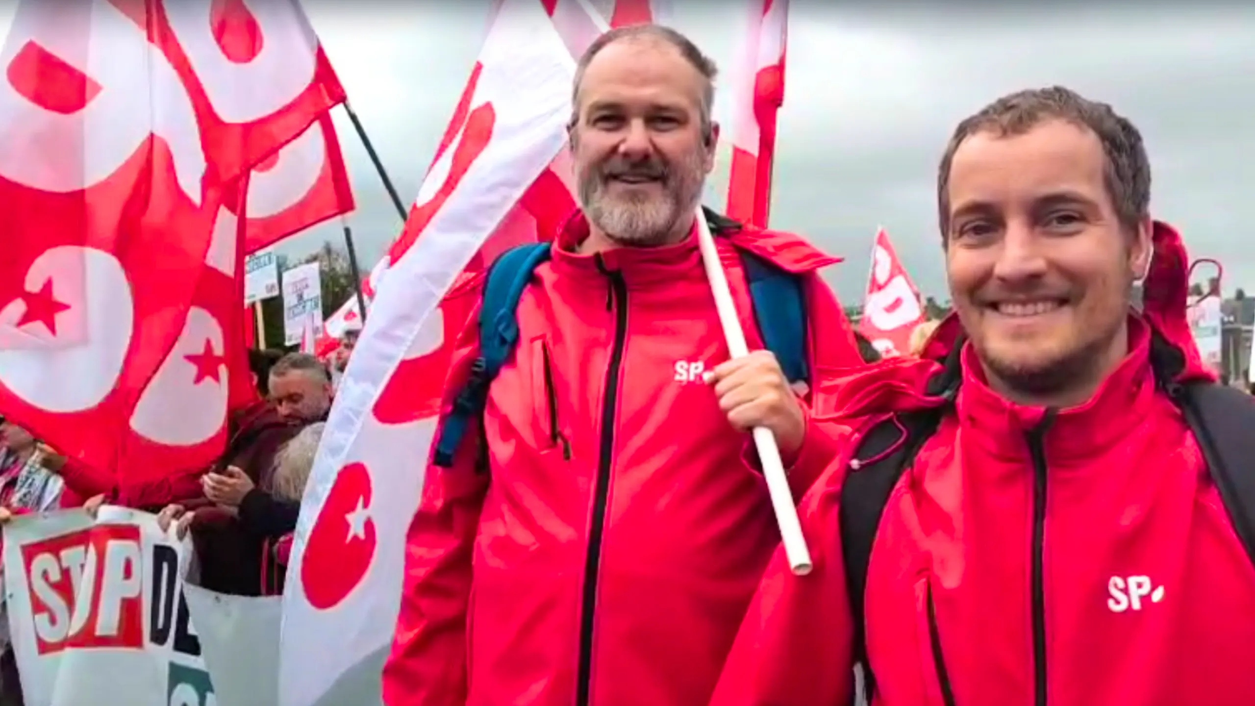 Voorzitter Willem de Vries en organisatiesecretaris Folkert Zeilemaker uit Alkmaar zijn op de Gazademonstratie in Amsterdam. Ze houden een vlag vast, hebben een SP-jas aan. Op de achtergrond een grote, rode menigte met SP-vlaggen.