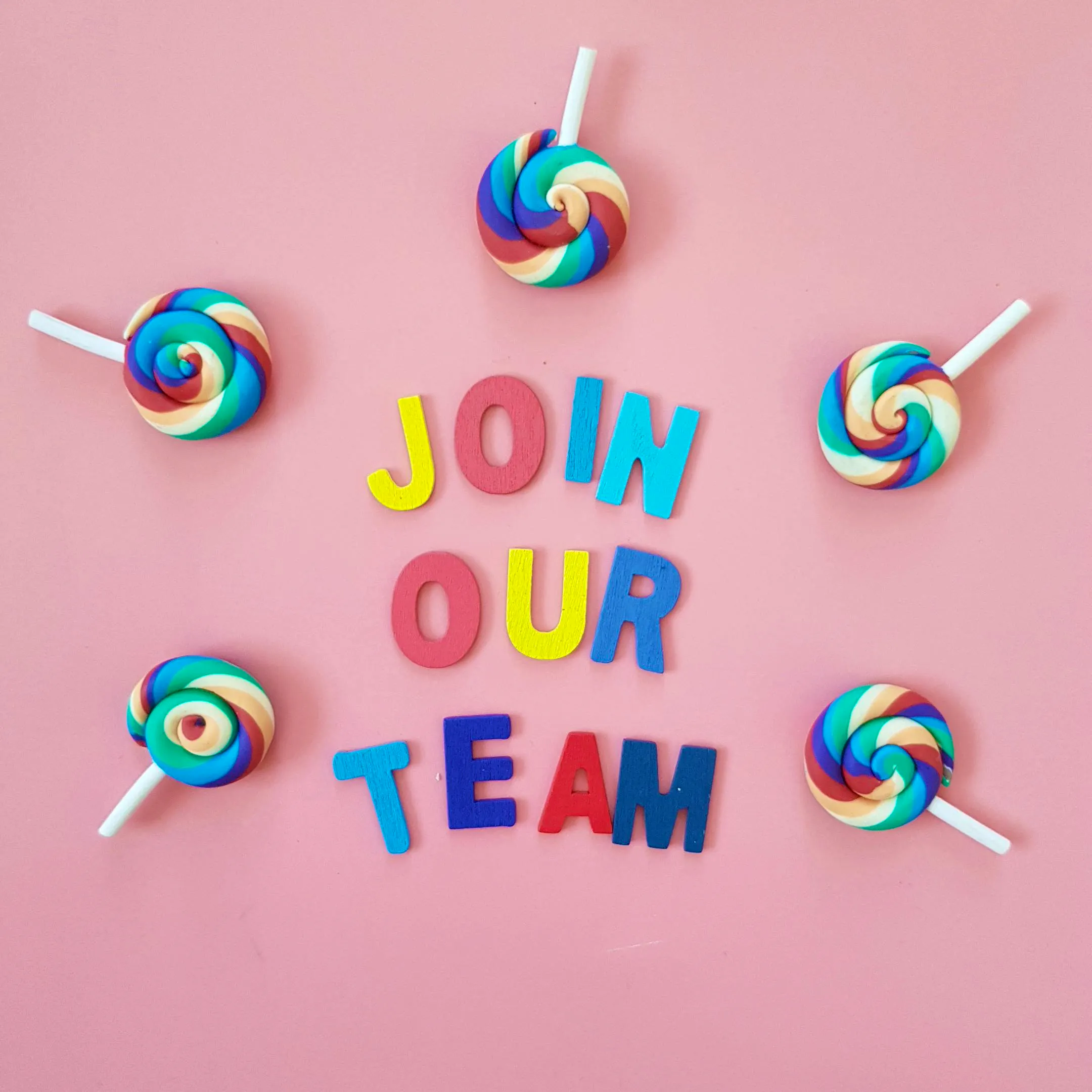 Een roze achtergrond met in het midden de letters: Join our team in regenboog kleuren. Rondom de letters liggen lolly's in regenboogkleuren.
